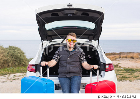 Travel, tourism and trip concept - young man sitting in open car trunk with two suitcases and 47331342