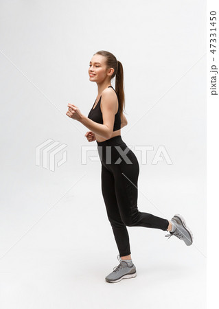 Full length picture of a sports woman running in studio over gray background. 47331450