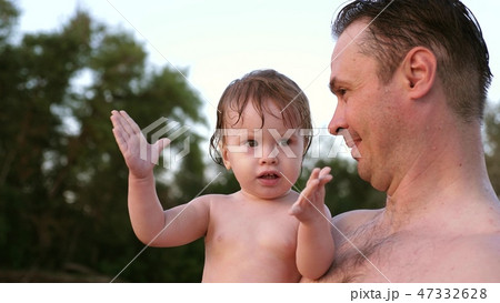 Small wet bathing child claps his hands and laughs sitting in embrace of dad 47332628
