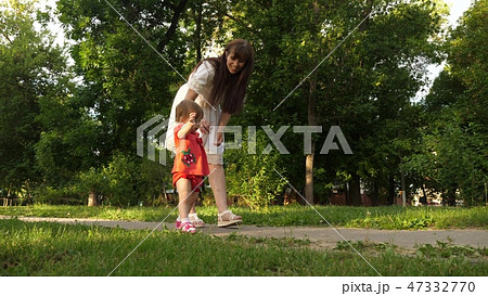Mom and little daughter are walking along path in the summer park. baby's first steps with mom Mom and little daughter are walking along path in the summer park. baby's first steps with mom 47332770