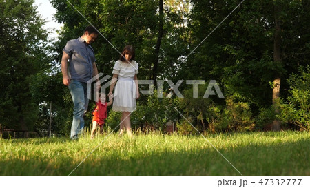Baby mom and dad are walking around holding hands and playing in city park on lawn grass. Baby mom and dad are walking around holding hands and playing in city park on lawn grass. 47332777