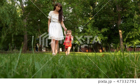 child and mother walk on green lawn grass in the summer city Park and smiling. child and mother walk on green lawn grass in the summer city Park and smiling. 47332791
