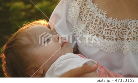 a small child falls asleep in arms of the mother, mother and daughter are walking in the summer park 47333155