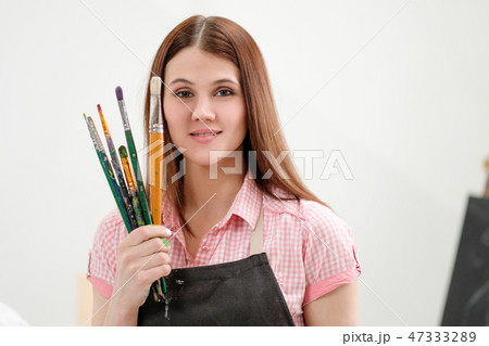 Young woman artist with brushes and paints in a white studio. Young woman artist with brushes and paints in a white studio. 47333289