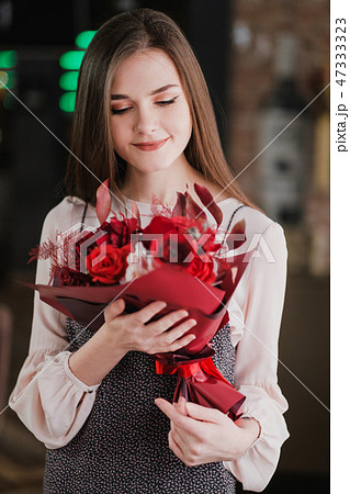 The girl is sitting in a cafe with a bouquet of red flowers, peonies, roses and chrysanthemums. The girl is sitting in a cafe with a bouquet of red flowers, peonies, roses and chrysanthemums. 47333323