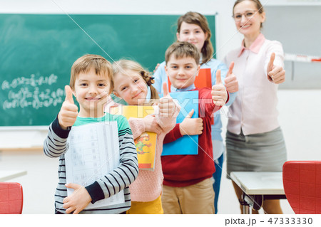 Pupils and teacher showing thumbs-up in school having fun 47333330
