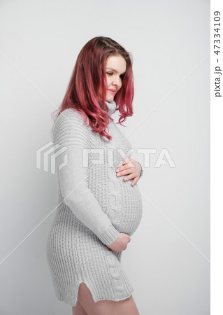 A pregnant woman with colored crimson hair in a knitted gray pullover. 47334109