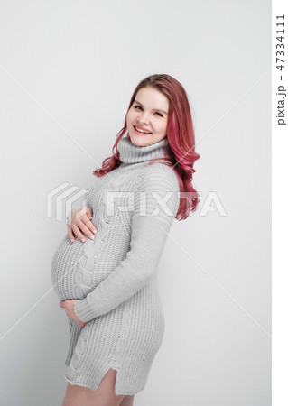 A pregnant woman with colored crimson hair in a knitted gray pullover. A pregnant woman with colored crimson hair in a knitted gray pullover. 47334111