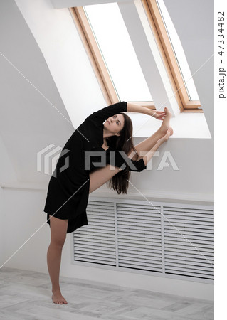 A young female dancer in a black dress is stretching by the window. White Hall, the working class A young female dancer in a black dress is stretching by the window. White Hall, the working class 47334482