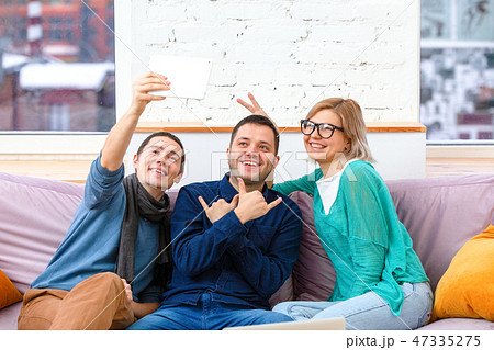 Friends sit on the couch, chatting and using a smartphone, desktop computer, laptop. 47335275