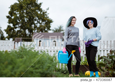 Two young women in the background of a garden with gloves and tools with a field of beds Two young women in the background of a garden with gloves and tools with a field of beds 47336087
