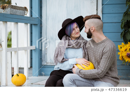 Young woman and man, family, sitting on porch of village house with pumpkins. Young woman and man, family, sitting on porch of village house with pumpkins. 47336619