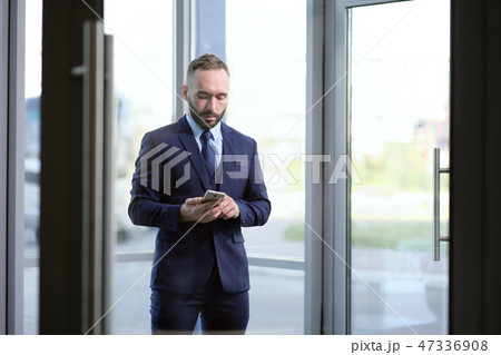 Handsome male businessman uses a smartphone on the background of an office building. Handsome male businessman uses a smartphone on the background of an office building. 47336908