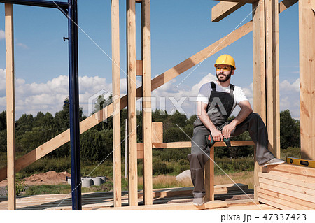 The man is a builder on the roof of a wooden frame house. The man is a builder on the roof of a wooden frame house. 47337423