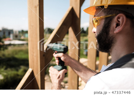 The man is a builder on the roof of a wooden frame house. 47337446