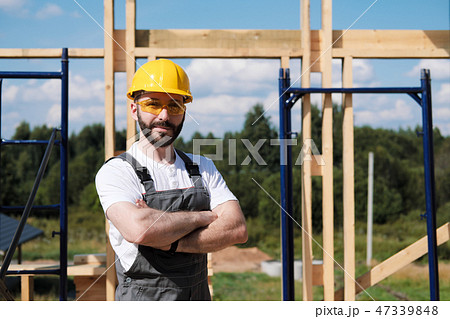 The man is a builder on the roof of a wooden frame house. 47339848