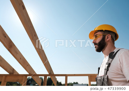 The man is a builder on the roof of a wooden frame house. 47339900