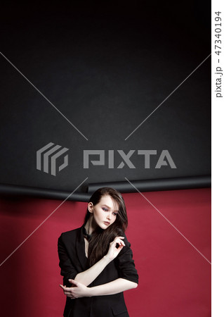 Portrait of a beautiful model girl in a business suit on a ragged red and black background. Hands 47340194