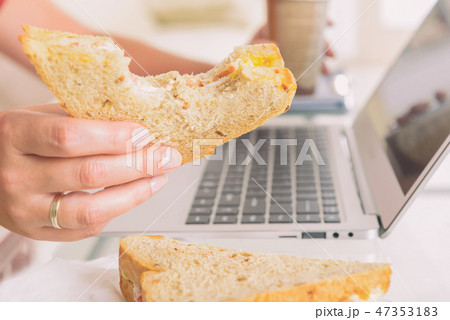Woman eating a breakfast sandwich while working 47353183