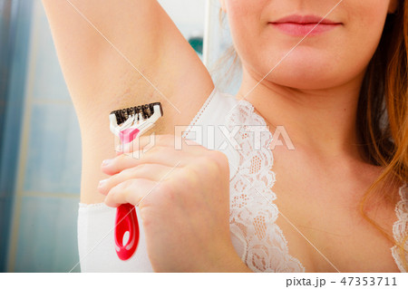 Woman shaving armpit with razor in bathroom 47353711