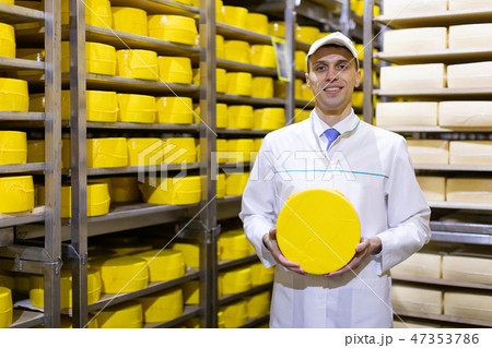 man in a white robe with a head of cheese in his hands is in a cheese warehouse 47353786