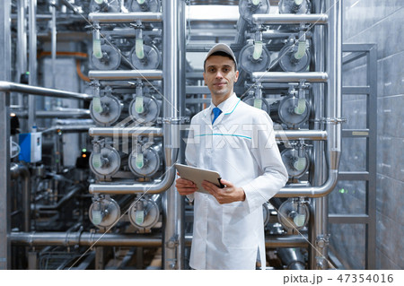 man in a white robe with a tablet in his hands is in the production shop at the factory man in a white robe with a tablet in his hands is in the production shop at the factory 47354016