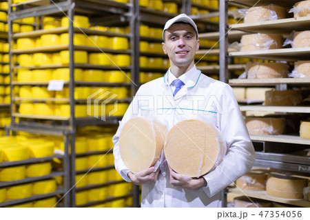man in a white robe with a head of cheese in his hands is in a cheese warehouse man in a white robe with a head of cheese in his hands is in a cheese warehouse 47354056