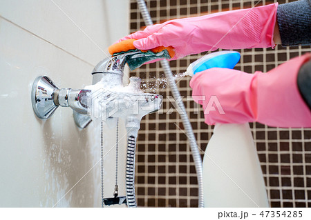 Image of hands in pink rubber gloves washing bathtub mixer 47354285