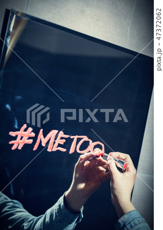 Girl writing "#metoo" on a mirror with a red lipstick. Girl writing "#metoo" on a mirror with a red lipstick. 47372062