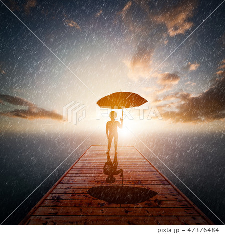 Child with umbrella standing alone wooden jetty in rain looking at the sea. 47376484