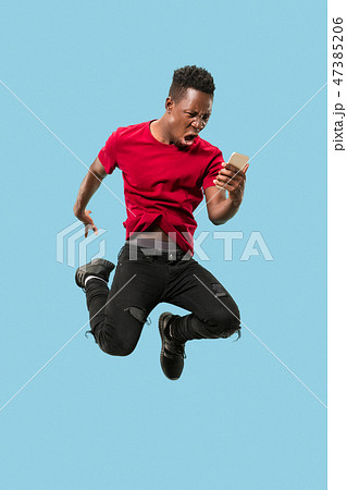 always on mobile. Full length of handsome young man taking phone while jumping 47385206