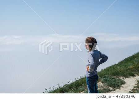 Boy stands on a mountain and looking at a thick fog. Boy stands on a mountain and looking at a thick fog. 47390346