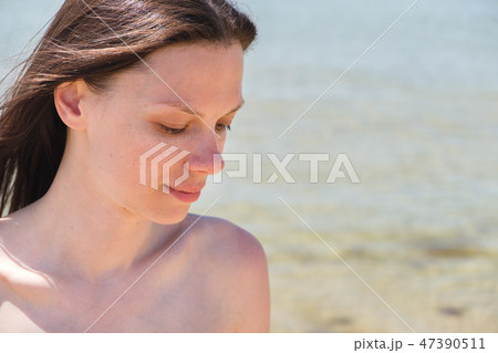 Closeup portrait with shoulders of brunette with long hair on the beach. The eyes are closed. Closeup portrait with shoulders of brunette with long hair on the beach. The eyes are closed. 47390511
