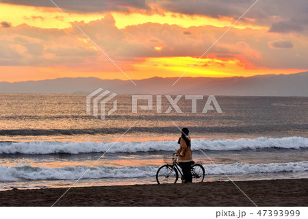 鵠沼海岸の夕焼けに染まる空と自転車の女性 鵠沼海岸の夕焼けに染まる空と自転車の女性 47393999
