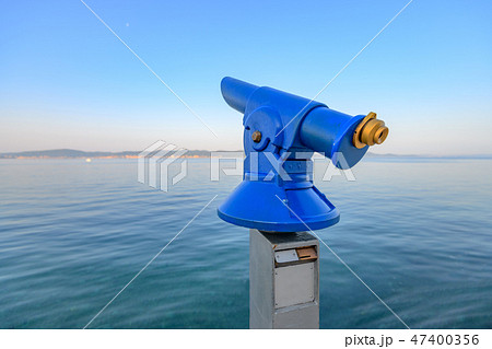 Blue public coin operated telescope, sea and island in background 47400356
