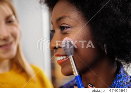 Fair-haired smiling stylist trying new look on the dark-skinned model Fair-haired smiling stylist trying new look on the dark-skinned model 47406645