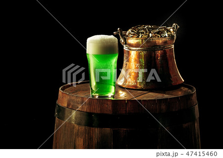 The wooden background with lots of gold coins and a large mug of beer with a green bow. 47415460