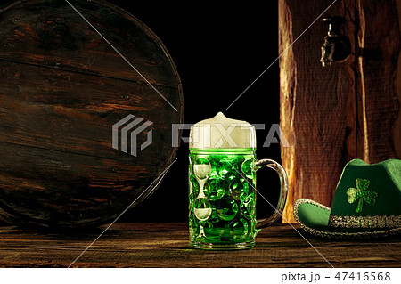 The wooden background with lots of gold coins and a large mug of beer with a green bow. 47416568