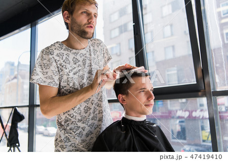 hairdresser does hair with comb of handsome satisfied client in professional hairdressing salon 47419410