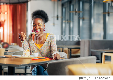 Cheerful African-American woman eating sweet pie in cafeteria Cheerful African-American woman eating sweet pie in cafeteria 47422587
