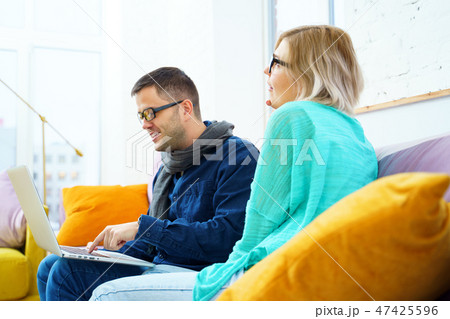 Man and woman sit on the couch, chatting and using a desktop computer. 47425596