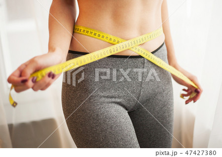 Hands measuring waist with a tape. Slim and healthy woman at her home Hands measuring waist with a tape. Slim and healthy woman at her home 47427380