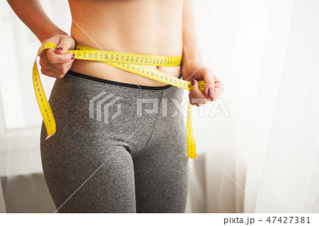 Hands measuring waist with a tape. Slim and healthy woman at her home 47427381
