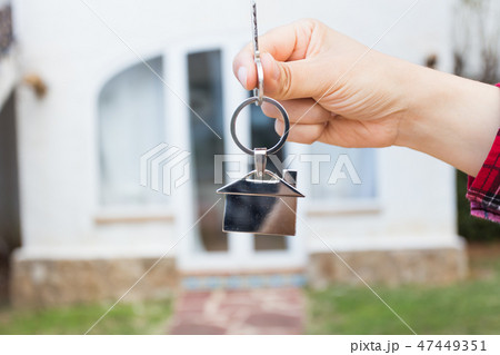 Real estate and property concept - Hand is holding house keys on house shaped keychain in front of a Real estate and property concept - Hand is holding house keys on house shaped keychain in front of a 47449351