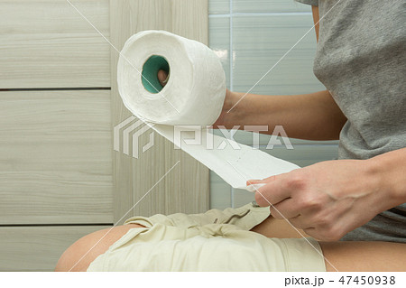 The girl is sitting on the toilet and tearing a piece of toilet paper 47450938