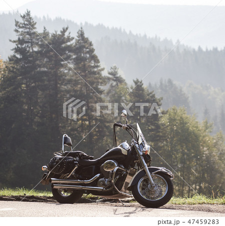 Black shiny high-speed motorcycle parked on empty narrow country roadside on sunny summer day. 47459283