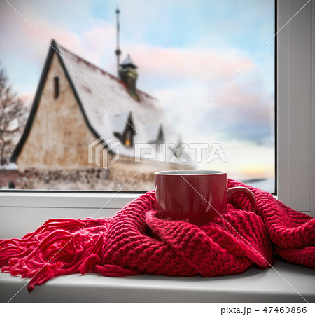 Cup of hot coffee or tea is wrapped with a scarf on the windowsill Cup of hot coffee or tea is wrapped with a scarf on the windowsill 47460886