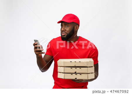 Delivery Concept: Handsome african pizza delivery man talking to mobile with shocking facial Delivery Concept: Handsome african pizza delivery man talking to mobile with shocking facial 47467092