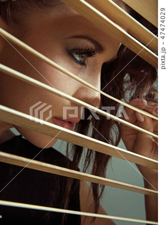 Young cute woman hiding herself behind blind Young cute woman hiding herself behind blind 47474029