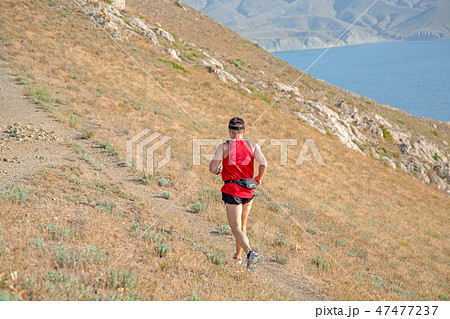 rear view of athletic runner running on a mountain trail on a blue sky background 47477237
